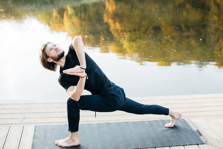 Young man doing yoga asana in the nature with the lake view. Evening workout outdoors, sports and healthy lifestyleの写真素材