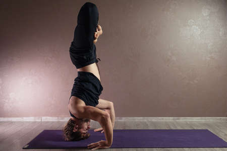Young sporty man practicing yoga, meditating in Half Lotus pose, working out, wearing sportswear, indoor full length, brown yoga studioの写真素材