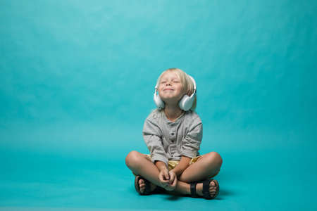 Very emotional boy listening to music on headphones on a blue background. The boy shows different emotions and he is happy. Musicの写真素材