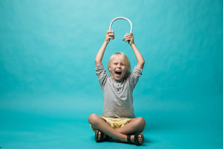 Very emotional boy listening to music on headphones on a blue background. The boy shows different emotions and he is happy. Musicの写真素材