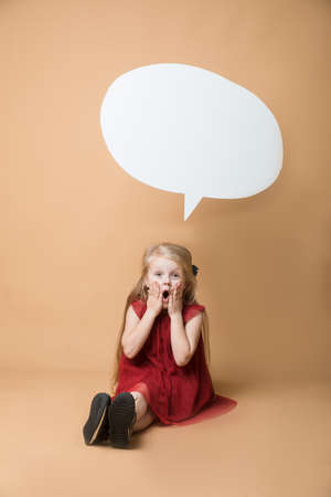Girl sit on the floor on an orange background. Girl is very happy. Of the girl hanging blank white speechの写真素材