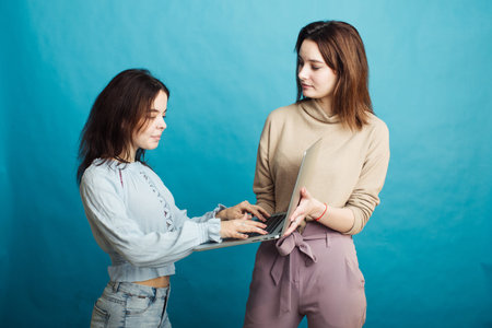 Image of happy young girls standing isolated over blue background and looking at laptopの写真素材