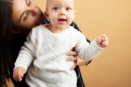 Young and energetic mom hugs and kisses her baby on orange background