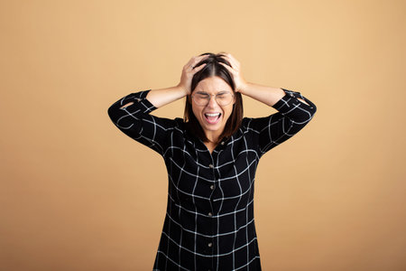 A young woman in a plaid dress stands on an orange background and shows different emotionsの写真素材