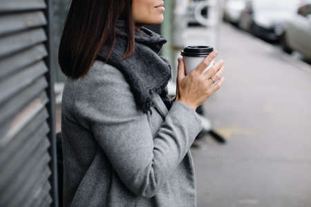 Portrait of a young woman in glasses. A young business woman stands at the window of a cafe and drinks coffeeの写真素材