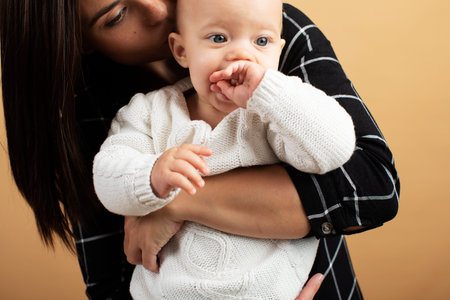 Young and energetic mom hugs and kisses her baby on orange background