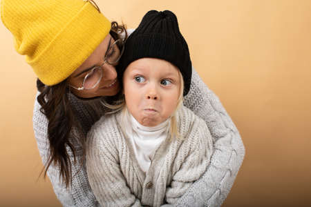 A young and energetic mother hugs and kisses her son on an orange backgroundの写真素材