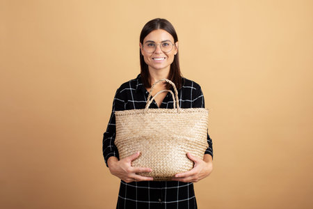 A young woman in a plaid dress stands with a wicker bag on an orange background