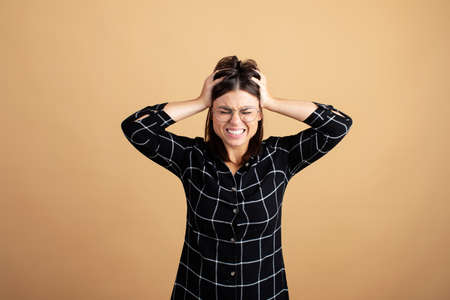 A young woman in a plaid dress stands on an orange background and shows different emotionsの写真素材