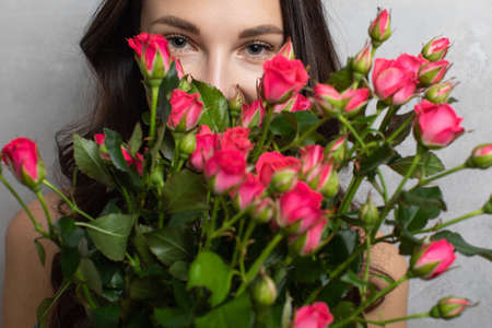 Close-up portrait of an attractive young woman in a summer dress holding a bouquet of roses looking at the cameraの写真素材