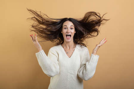 An image of a young beautiful woman in a white sweater posing on an isolated orange background shows different emotionsの写真素材