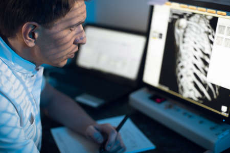 in medical laboratory patient undergoes MRI or CT scan process under Supervision of Radiologist in Control Room, He Watches Procedure and Monitors skeleton and ribs of the patientの写真素材