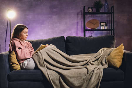 Young girl reading a book. The girl is lying on the couch. Cozy room. Girl dreamsの写真素材