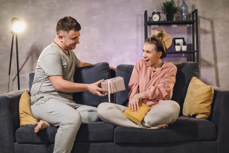Young family in a cozy apartment on the couch. The family is happy. The husband gives a gift to his wife.の写真素材