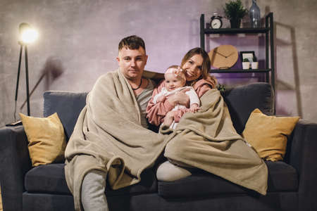 Young family sitting on the couch in a cozy room. Mom, dad and baby are happy. family watching TVの写真素材