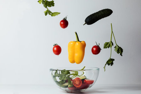 Healthy salad with flying vegetable ingredients on a white background. Cherry tomatoes, yellow...