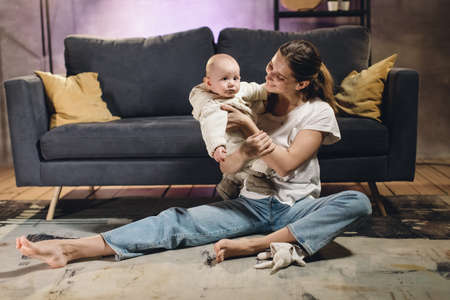A young girl is sitting on the carpet with her child in a cozy room. Mom and baby playの写真素材