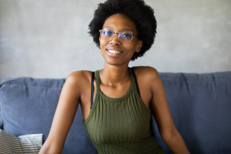 Happy african American young woman looking in camera sit relax on cozy couch happy to move to new...