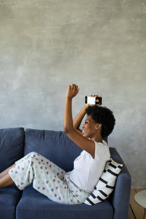 African American girl dancing with her phone on the couch in a cozy room