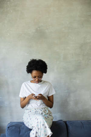 Happy african American young woman sit relax on cozy couch happy to move to new apartment. Smiling black girl rest on comfortable sofa in living room dreamingの写真素材
