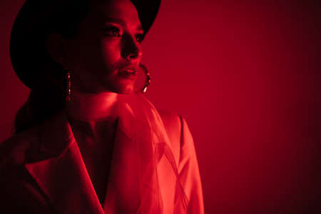 Young girl in a white suit and a black hat. The concept of clothing. Red light. Red backgroundの写真素材