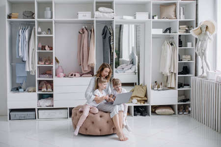 Young mother with her twin daughters choose things online in her cozy apartmentの写真素材