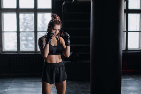 Athletic fit female boxer exercising punches with boxing bag in gym during kickboxing and self defense intensive workoutの写真素材