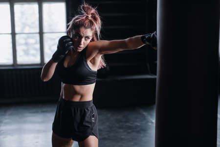 Athletic fit female boxer exercising punches with boxing bag in gym during kickboxing and self defense intensive workoutの写真素材