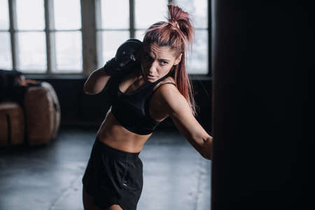 Athletic fit female boxer exercising punches with boxing bag in gym during kickboxing and self defense intensive workoutの写真素材