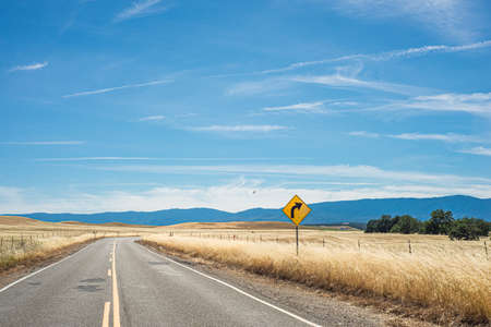 A rural road with a yellow curve sign in the Northern California countrysideの写真素材