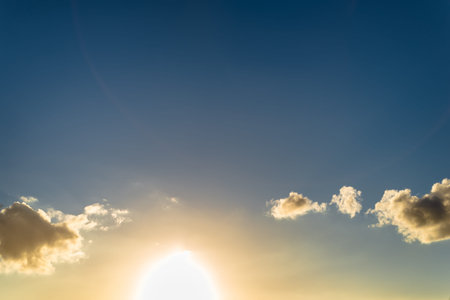 Beautiful fluffy dark clouds with sun setting behind them in the bottom of the frame. Simple, backlit, minimalistic photo with copy space.の写真素材