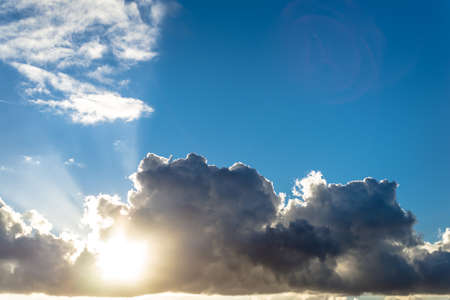Beautiful fluffy dark grey and white clouds, of varying thickness, with sun rays shining through from behind. Simple, backlit, minimalistic photo with copy space.の写真素材