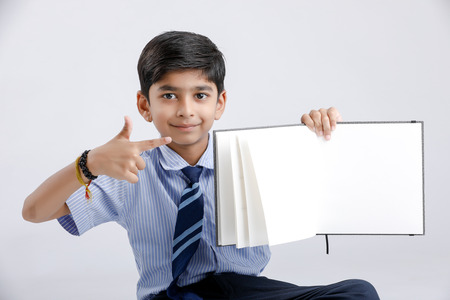 Cute little Indian/Asian school boy showing note book over white backgroundの写真素材