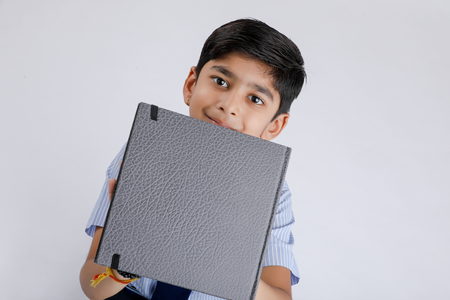 Cute little Indian/Asian school boy showing note book over white backgroundの写真素材