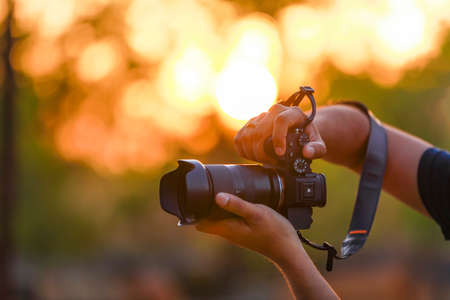 Jalgaon, Maharashtra / India - May 4, 2020 : Closeup of a black camera holding by Photographer's hand with sunset backgroundのeditorial素材