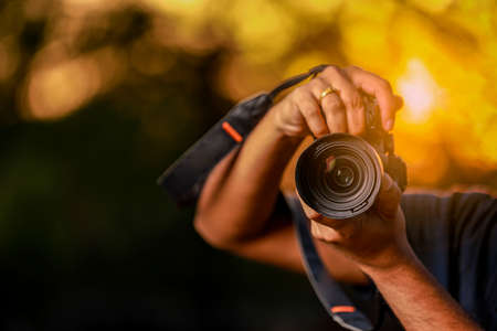Jalgaon, Maharashtra / India - May 4, 2020 : Closeup of a black camera holding by Photographer's hand with sunset backgroundのeditorial素材