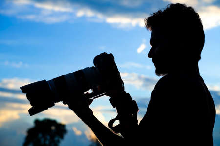 Silhouette of a man photographer with dslr camera during taking photos at sunsetの写真素材
