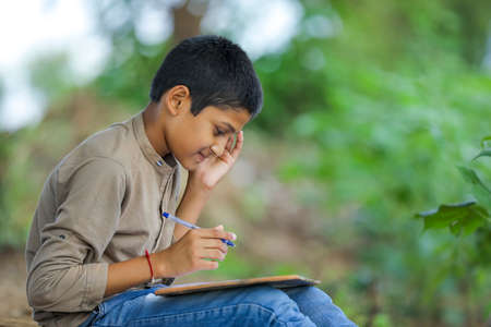 Cute little Indian/Asian boy showing writing pad pad with penの写真素材