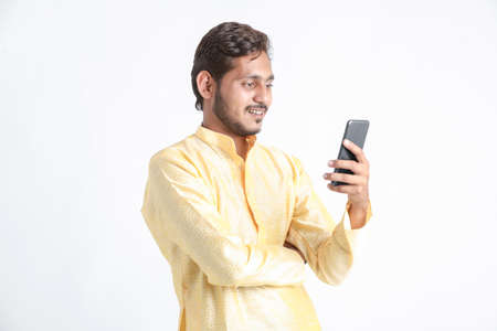 Young indian man in tradition wear and using smartphone on white background.の写真素材