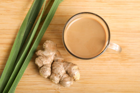 Glass cup of hot ginger tea with ginger rhizome (root) sliced isolated on wooden background.