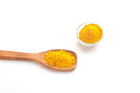 Turmeric powder in wooden spoon and glass bowl on white background.