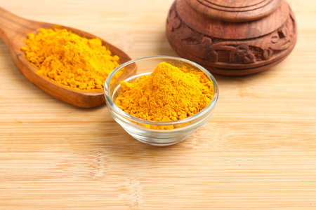 Turmeric powder in wooden spoon and glass bowl on white background.