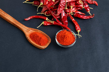 Dried red chilli and powder in glass bowl and wooden spoon on dark background.の写真素材