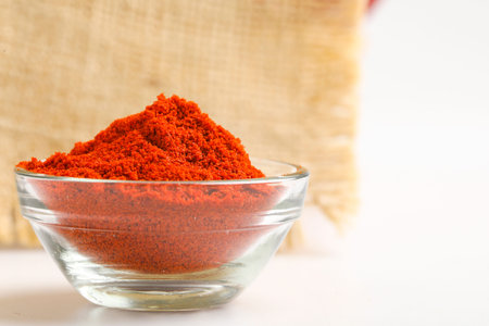 Dried red chilli and red chilli powder in glass bowl and wooden spoon on white backgroundの写真素材
