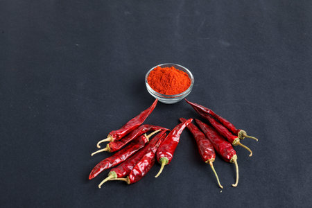 Dried red chilli and powder in glass bowl on dark background.