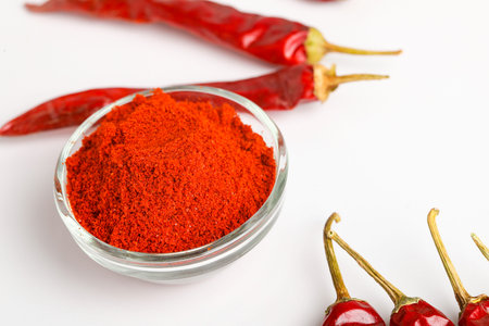 Dried red chilli and powder in glass bowl on white background.