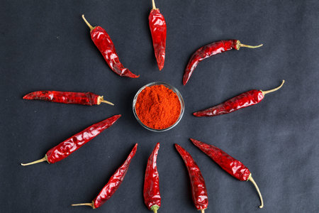 Dried red chilli and powder in glass bowl on dark background.