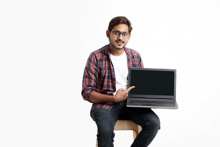 Indian college student showing laptop screen on white background.の写真素材