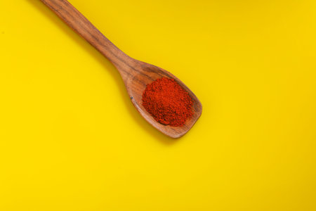 Chilli powder in wooden spoon with dry red chilly on yellow background.