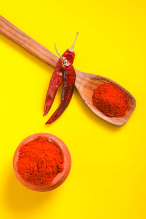 Chilli powder in wooden spoon with dry red chilly on yellow background.の写真素材